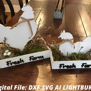May include: Two white wooden rooster and hen decorations with burlap accents, nestled in rectangular boxes filled with moss, faux nests, and eggs. The boxes are labeled "Fresh Farm" in black script, perfect for farmhouse decor.