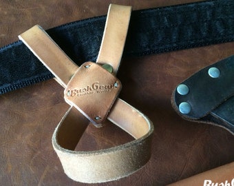 May include: A brown leather axe sheath with a black strap and a brown leather loop. The sheath has a metal rivet and the text "BushGear Leather Works" is embossed on the loop.