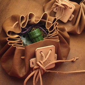 May include: Two brown leather pouches with drawstrings and a flap closure. The pouches are empty, but one has a small green tube inside.