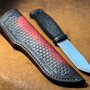 Könnte beinhalten: Eine schwarze Lederscheide für ein Messer mit einem roten und schwarzen Farbverlauf. Die Scheide hat ein dekoratives Stichmuster und ist für ein Messer mit schwarzem Griff konzipiert. Das Messer ist nicht im Bild enthalten.