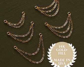 May include: Several gold-filled chain charms with multiple strands, perfect for jewelry making. The charms are arranged on a dark green surface. The image includes a circular emblem that reads "14K Gold-Fill Made in USA."