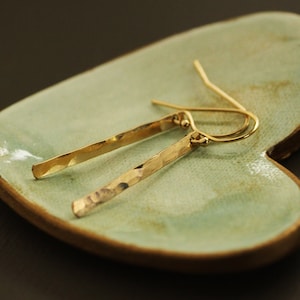 May include: A pair of gold hammered bar earrings with a simple wire hook closure.