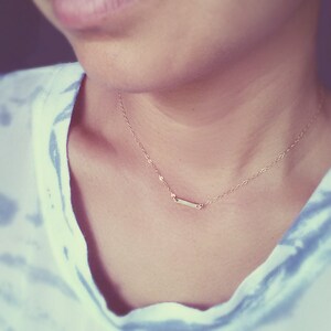 May include: A delicate gold chain necklace with a small, thin bar pendant.
