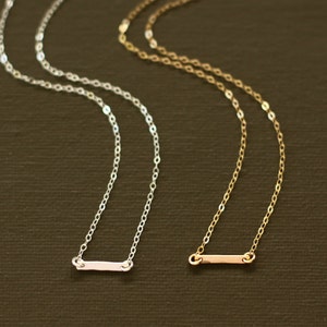 May include: Two delicate necklaces with a simple bar pendant. One necklace is silver and the other is gold.