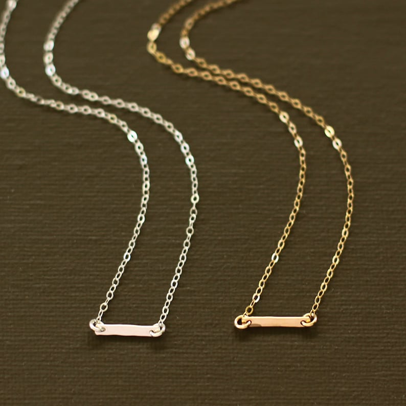 May include: Two delicate necklaces with a simple bar pendant. One necklace is silver and the other is gold.