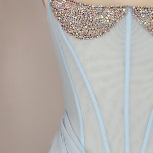 May include: A light blue strapless dress with a sheer bodice and a beaded neckline. The skirt is made of a soft, flowing fabric.