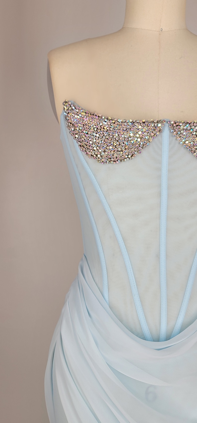 May include: A light blue strapless dress with a sheer bodice and a beaded neckline. The skirt is made of a soft, flowing fabric.