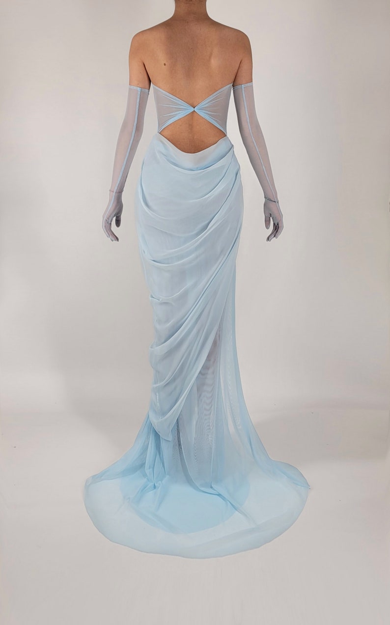 May include: A light blue, strapless gown with a low back and a flowing skirt. The gown is made of a sheer fabric and has a gathered detail at the waist.