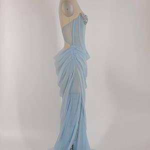 May include: A light blue, sheer, long, formal gown with a fitted bodice and a flowing skirt. The bodice has a sweetheart neckline and is adorned with rhinestones.