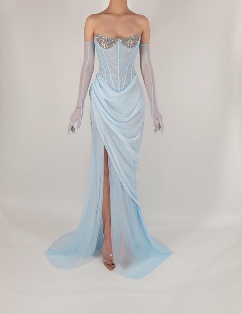May include: A light blue, strapless gown with a fitted bodice and a flowing skirt. The bodice is embellished with a crystal design. The gown has a thigh-high slit and a long train.