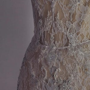 May include: A white lace dress with a sweetheart neckline and a fitted bodice. The dress is covered in small, sparkling beads and has a sheer, flowing skirt.