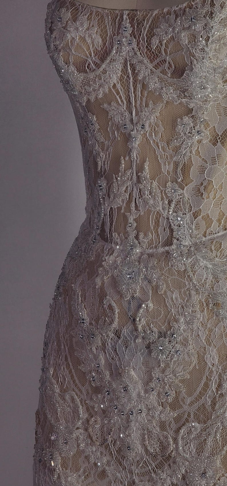 May include: A white lace dress with a sweetheart neckline and a fitted bodice. The dress is covered in small, sparkling beads and has a sheer, flowing skirt.