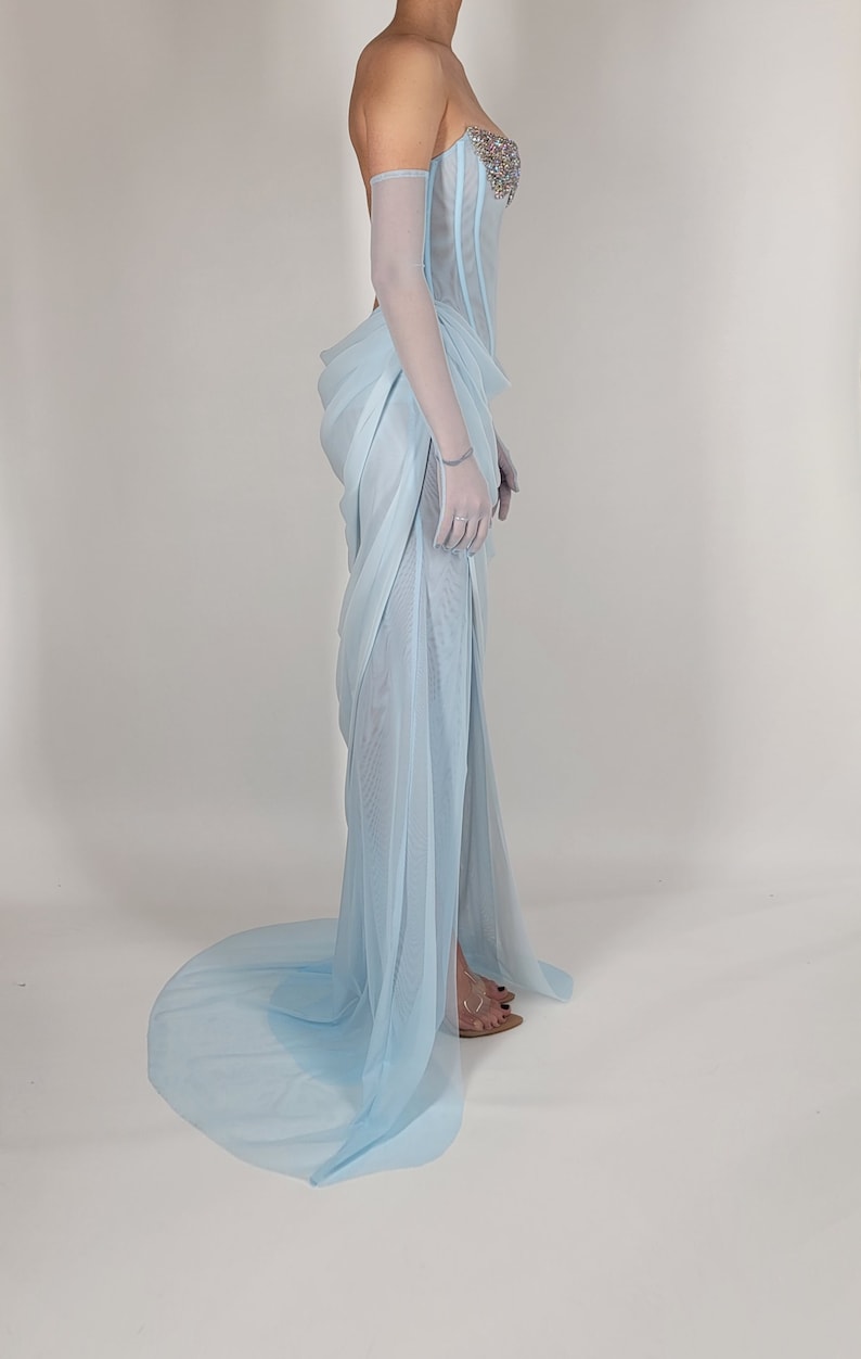 May include: A light blue sheer gown with a fitted bodice and a flowing skirt. The bodice has a beaded embellishment.
