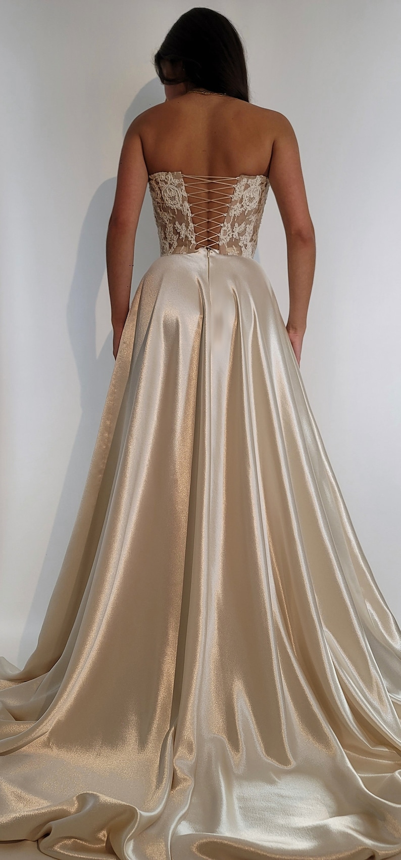 May include: A strapless, ivory satin gown with a lace bodice and a corset back. The skirt is full and flowing.