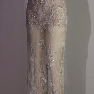 May include: A white, sheer, beaded lace gown with a fitted bodice and a flowing skirt.