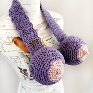 May include: Purple crocheted breast forms with pink crocheted nipples. The forms are attached to a purple crocheted strap.