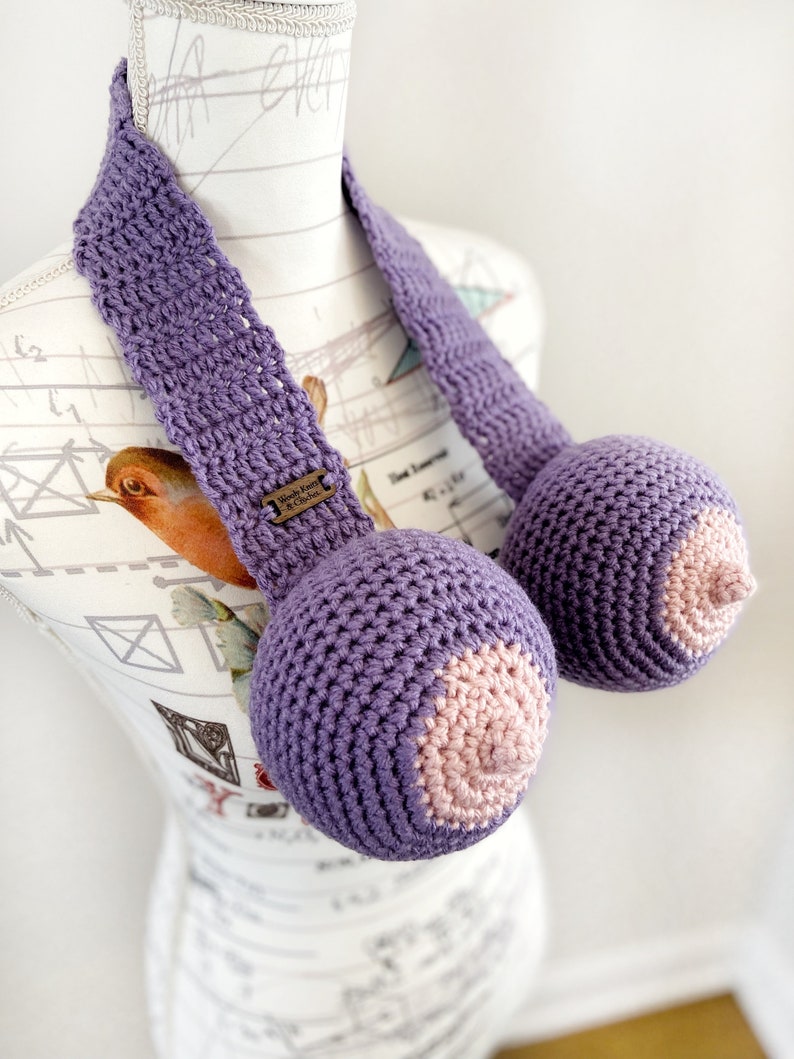 May include: Purple crocheted breast forms with pink crocheted nipples. The forms are attached to a purple crocheted strap.