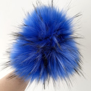 May include: A vibrant blue faux fur pompom with black tips. The fluffy accessory is against a white background. This item could be used for hats, scarves, or other craft projects.