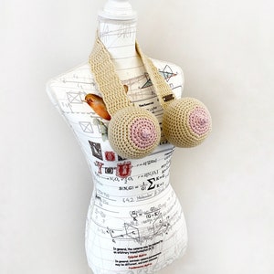 May include: A crocheted bra with beige straps and pink crocheted cups. The bra is displayed on a white mannequin with a printed pattern.