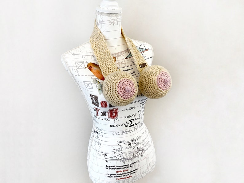 May include: A crocheted bra with beige straps and pink crocheted cups. The bra is displayed on a white mannequin with a printed pattern.