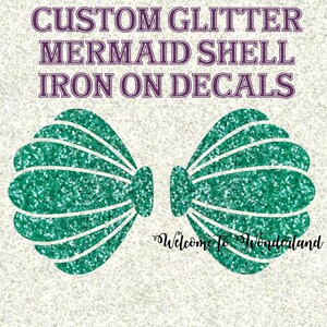 May include: Custom glitter mermaid shell iron-on decals. The design features two teal glitter shell shapes with white outlines, arranged symmetrically. The text "Welcome to Wonderland" is written in a cursive font below the shells. The background is a light, textured pattern.