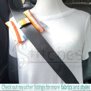 May include: Seat belt cover with colorful striped fabric in orange, white, and blue. The cover is attached to a black seat belt. The text "Check out my other listings for more fabrics and styles" is at the bottom of the image.