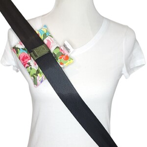 May include: A black seatbelt with a floral patterned fabric cushion attached to it. The cushion is secured to the seatbelt with a green strap.
