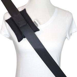 May include: Black seat belt shoulder pad with a black seat belt. The pad is made of a soft material and is designed to provide comfort and protection. The seat belt is angled across the chest.