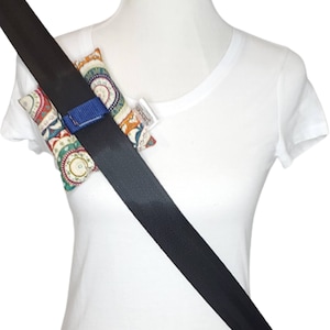 May include: Seat belt shoulder pads with a colorful paisley pattern. The pads are attached to a black seat belt with a blue strap. The pads are designed to provide comfort and reduce irritation from the seat belt.