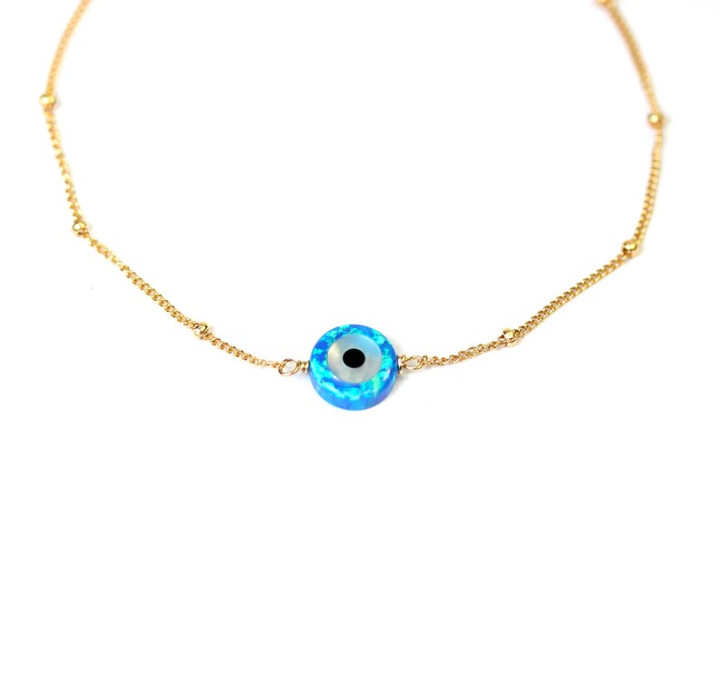 May include: A gold chain necklace with a blue and white evil eye charm. The charm is round and has a black pupil.