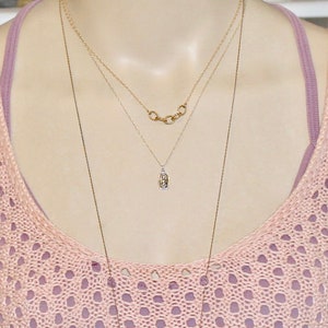 May include: A woman wearing a pink crocheted top with two necklaces. One necklace is a delicate silver chain with a small pendant, and the other is a gold chain with multiple linked circles.