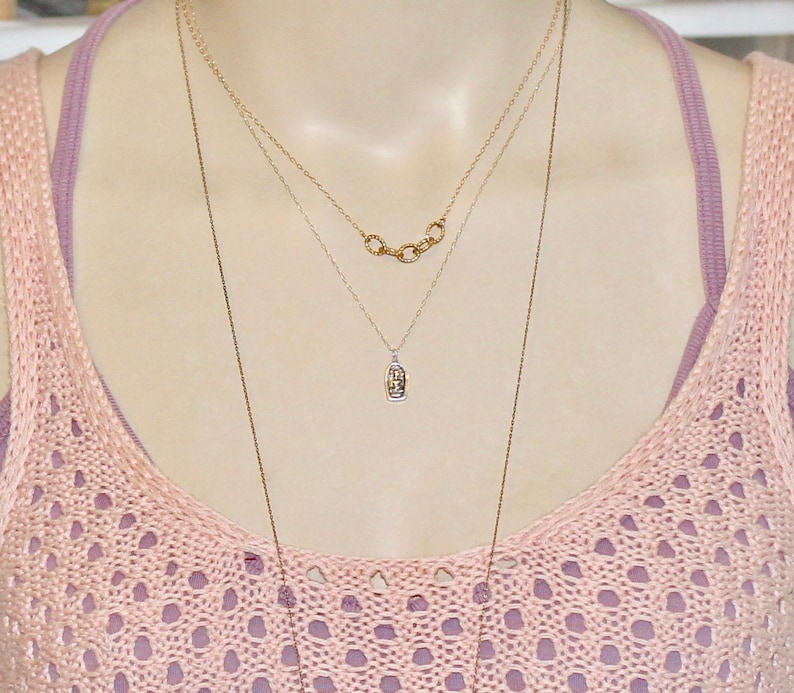 May include: A woman wearing a pink crocheted top with two necklaces. One necklace is a delicate silver chain with a small pendant, and the other is a gold chain with multiple linked circles.
