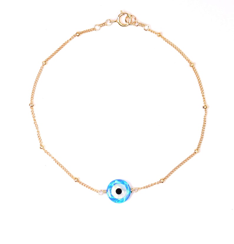 May include: A gold chain bracelet with a blue evil eye charm. The chain has small gold beads.