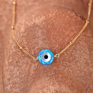 May include: A gold chain necklace with a blue and white evil eye charm. The charm has a black pupil and a white iris.