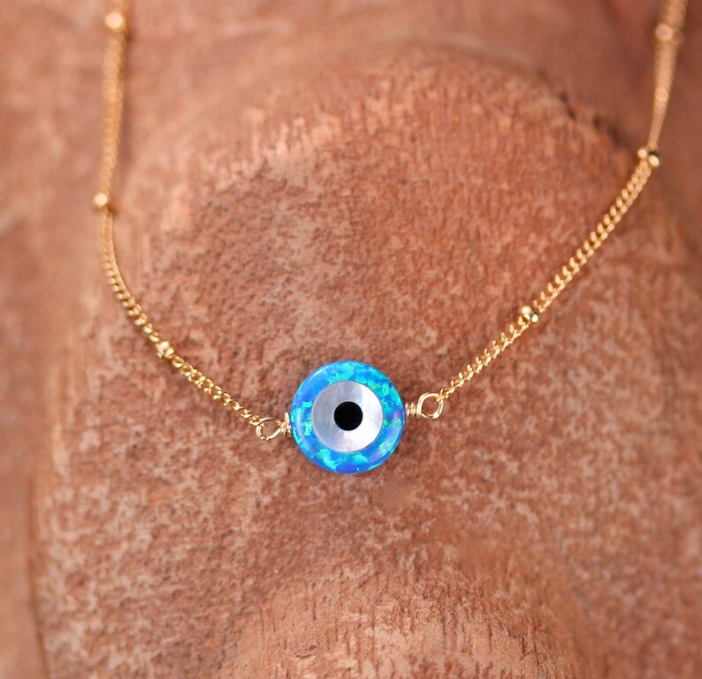 May include: A gold chain necklace with a blue and white evil eye charm. The charm has a black pupil and a white iris.