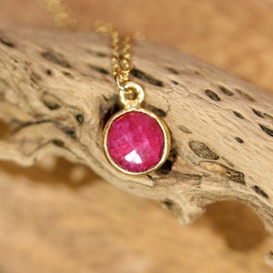 May include: A gold chain necklace with a round, red ruby pendant.