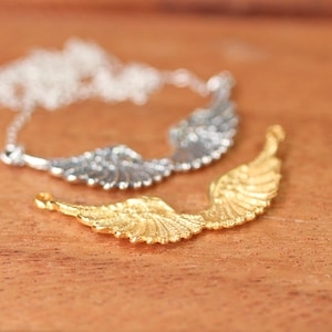 Puede incluir: Dos abalorios con forma de alas de &aacute;ngel, uno plateado y otro dorado, sobre una superficie de madera. El abalorio dorado est&aacute; enfocado y el plateado est&aacute; desenfocado.