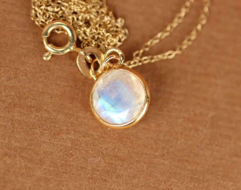 May include: A gold chain necklace with a round, iridescent moonstone pendant.