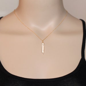 May include: A gold chain necklace with a clear quartz crystal pendant. The pendant is a long, thin, pointed shape.