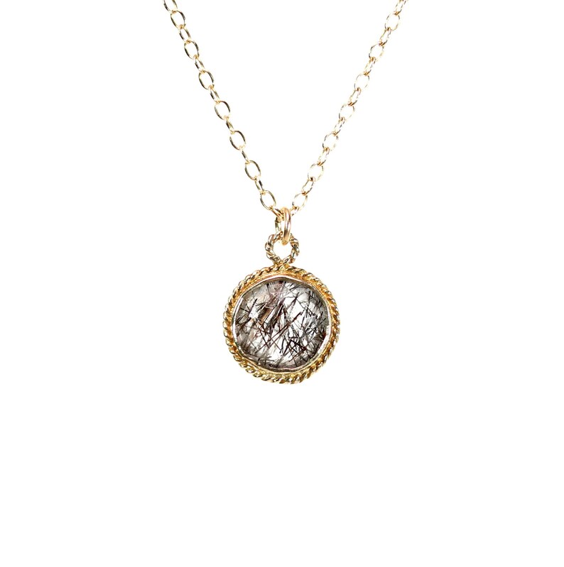 May include: A gold chain necklace with a round pendant featuring a clear quartz stone with black inclusions. The pendant has a rope-like gold border.