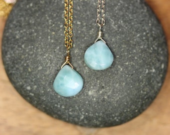 Könnte beinhalten: Zwei Halsketten mit facettierten, tropfenförmigen hellblauen Larimar-Edelsteinen. Ein Anhänger hängt an einer goldfarbenen Kette, der andere an einer silberfarbenen Kette. Jeder Stein ist oben mit einer Drahtwicklung sicher befestigt.