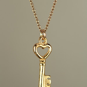 Puede incluir: Un collar de oro con un colgante de llave en forma de coraz&oacute;n.
