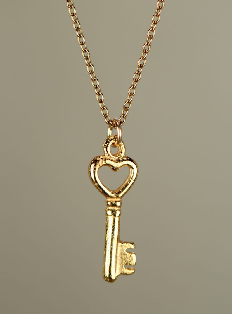 Puede incluir: Un collar de oro con un colgante de llave en forma de coraz&oacute;n.