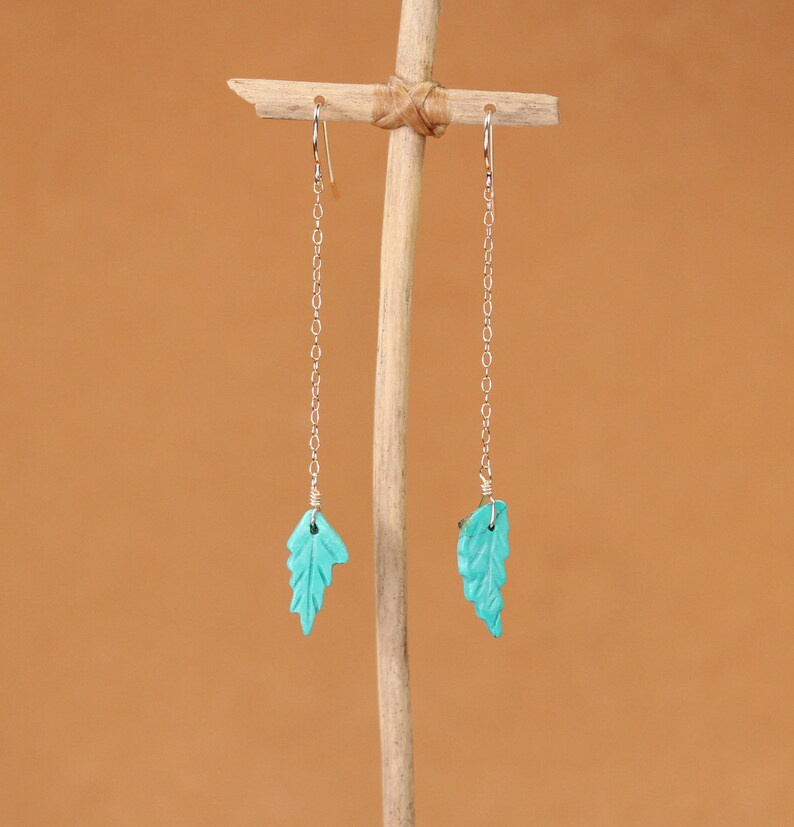 May include: A pair of silver dangle earrings with turquoise leaf-shaped charms.