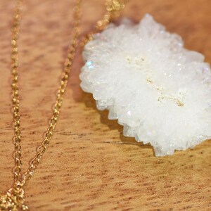 May include: A gold chain necklace with a white crystal pendant. The crystal is a cluster of small, white crystals.