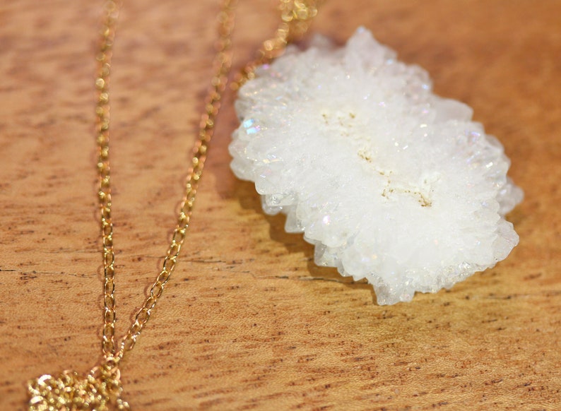 May include: A gold chain necklace with a white crystal pendant. The crystal is a cluster of small, white crystals.