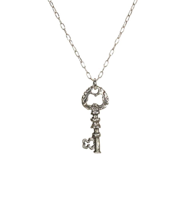 Puede incluir: Un collar de plata con un colgante de llave adornado. La llave tiene un dise&ntilde;o detallado y un gran ojo de cerradura.