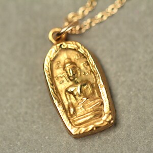 May include: Gold pendant necklace featuring a detailed image of a seated Buddha figure. The pendant is oval shaped and has a decorative border.