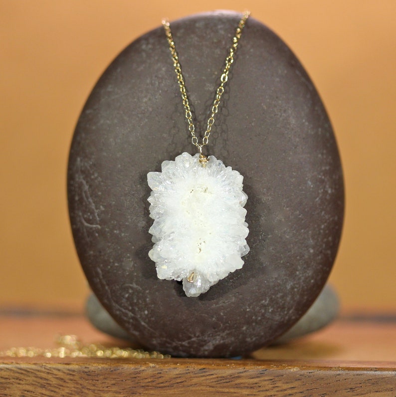 May include: A delicate gold chain necklace featuring a white quartz crystal pendant. The crystal is a cluster of small, pointed crystals forming a unique and natural shape.