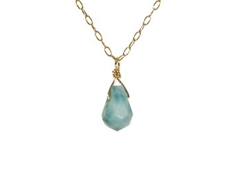 Könnte beinhalten: Halskette mit goldfarbener Kette und einem tropfenförmigen, facettierten, hellblauen Edelstein-Anhänger. Der Anhänger wird von einer goldenen Drahtfassung gehalten. Ein zarter Schmuck.